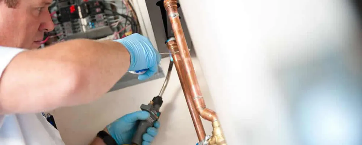 Water heater repair technician testing copper pipe connections and controls in Bakersfield, CA