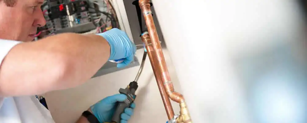 Water heater repair technician testing copper pipe connections and controls in Bakersfield, CA